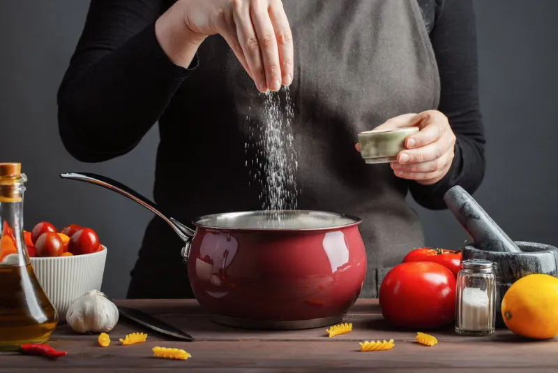 the chef preparations spaghetti and pasta, salt water, against a dark background, the concept of cooking woman salting water before cooking pasta fusilli