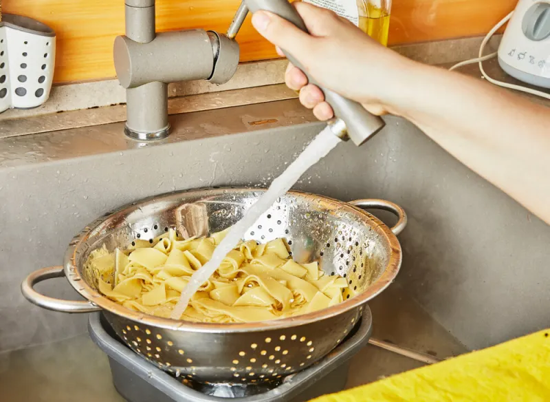 teenager rinses pasta under running water for spaghetti bolognese according to recipe from the internet