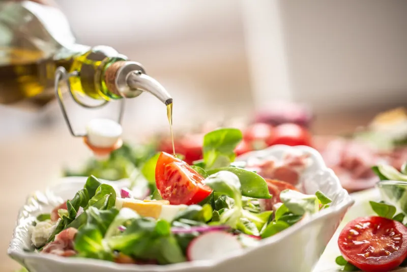 bottle with olive oil pouring into salad
