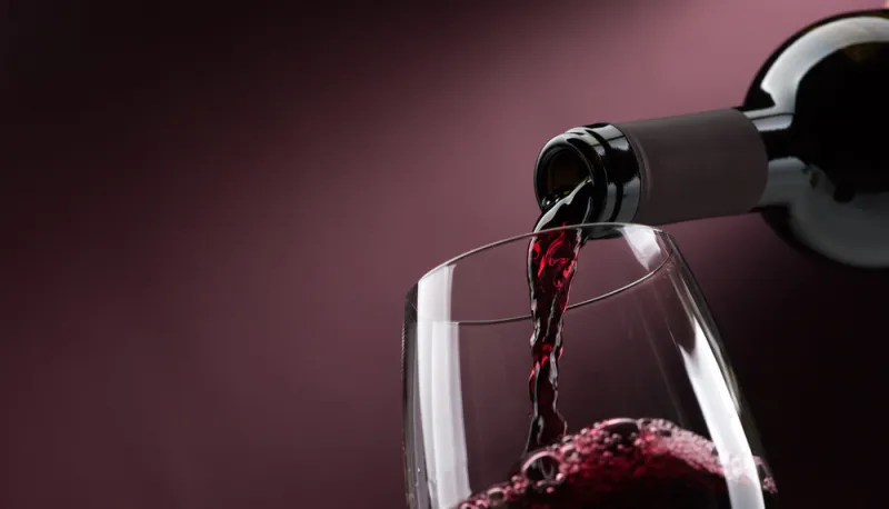 pouring red wine from a bottle into a wineglass  wine tasting and celebration