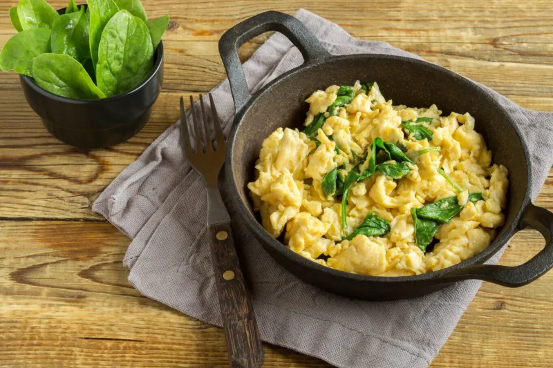 scrambled eggs with spinach in a cast-iron pan on a wooden table