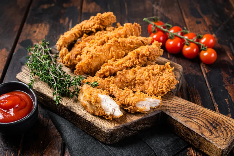 crispy fried breaded chicken strips, breast fillet meat with tomato ketchup on a plate wooden backgrund top view