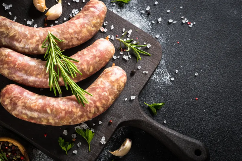 bratwurst or sausages on cutting board with spices at black table top view with copy space