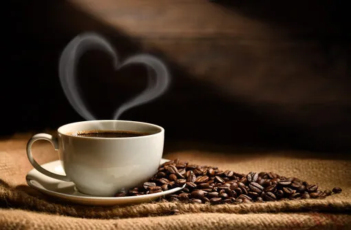 cup of coffee with heart shape smoke and coffee beans on burlap sack on old wooden background