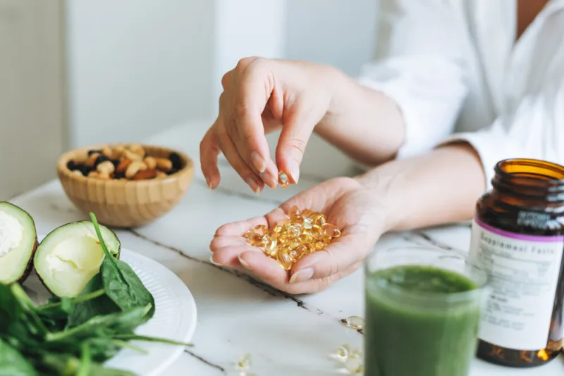 woman doctor nutritionist hands in white shirt with omega 3, vitamin d capsules with green vegan food the doctor prescribes a prescription for medicines and vitamins at the clinic, healthy food and treatment