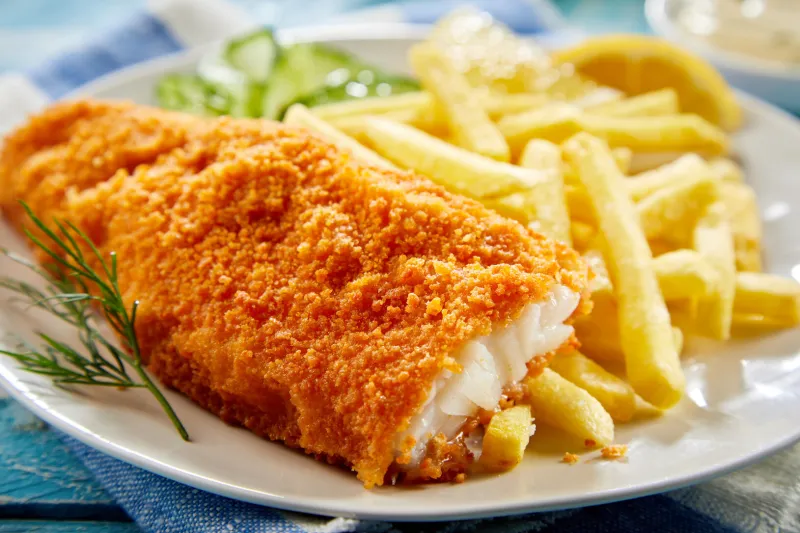 portion of crispy breaded fish fillet with french fries served on plate