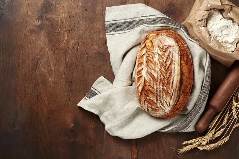freshly baked artisan sourdough bread loaves with wheat spike and bag of flour on dark wooden background top view with copy space