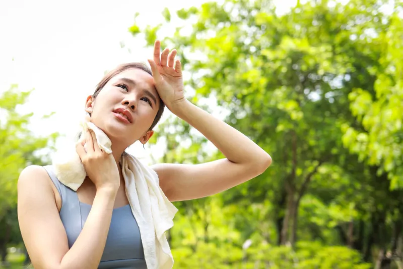 asian woman exercising outdoors on a hot sunny day with her body temperature above 40 degrees celsius she wipes her sweat with a towel heat stroke concept copy space