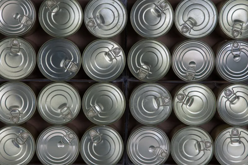 food behind sheet metal lined up tin cans with pull-off lids viewed from above