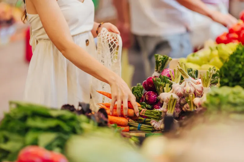 female hands puts fruits and vegetables in cotton produce bag at food market reusable eco bag for shopping zero waste concept