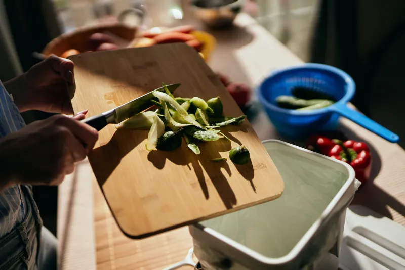 the cook preparing healthy green salad for lunch and recycling organic leftovers in a compost bin female person throwing cucumber peels in a bokashi container sustainable lifestyle concept