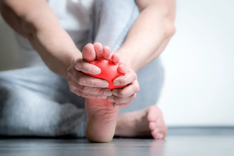 causian man holds hands to his painful feet, pain in foot, red color is area of pain