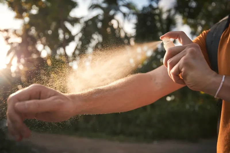 man is applying insect repellent on his hand against palm trees prevention against mosquito bite in tropical destination