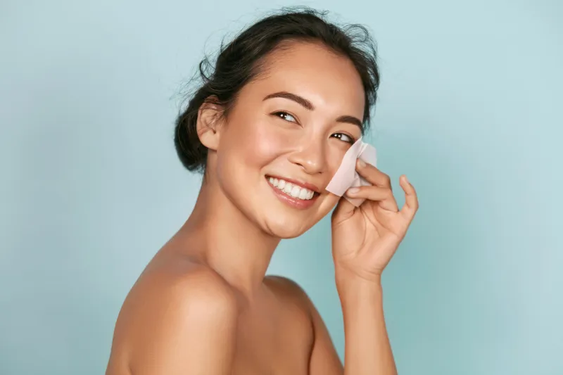 face skin care smiling woman using facial oil blotting paper portrait closeup of beautiful happy asian girl model with natural makeup using oil absorbing sheets, beauty product at studio