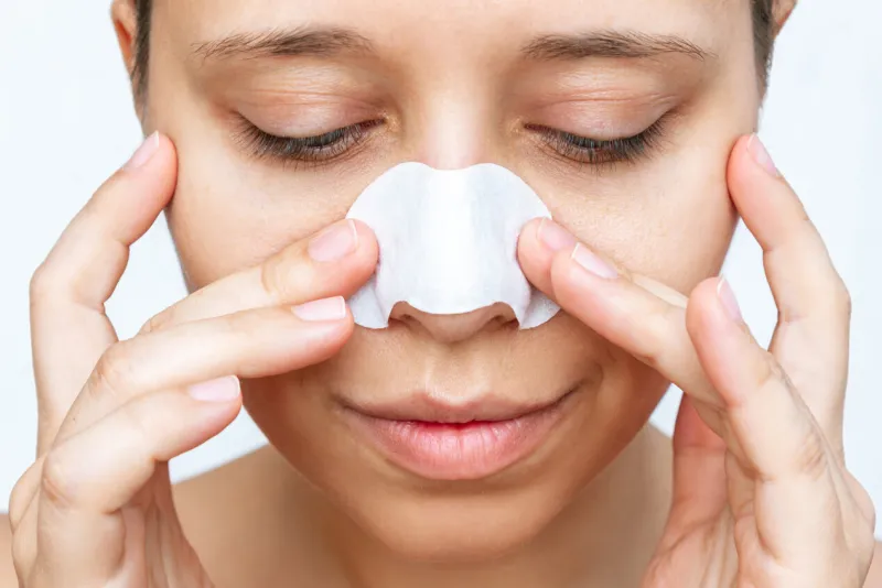 young woman cleaning the skin of her nose with strips from black