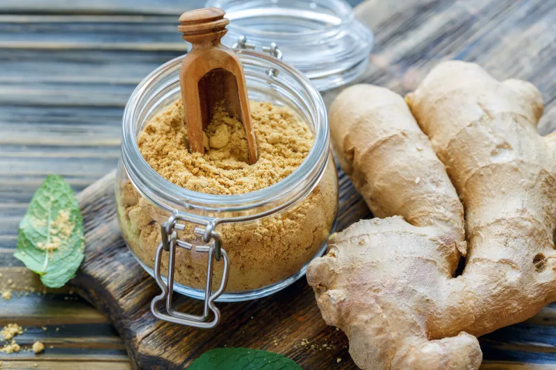 jar with ground ginger and fresh ginger root on old wooden table, selective focus