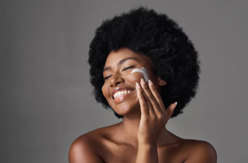 beauty, skin care and black woman with lotion on face, afro and cosmetics in studio on grey background natural skincare, collagen cream and african model with salon glow, dermatology and wellness