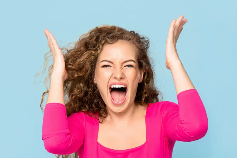shocked angry young caucasian woman shouting isolated on light blue studio background