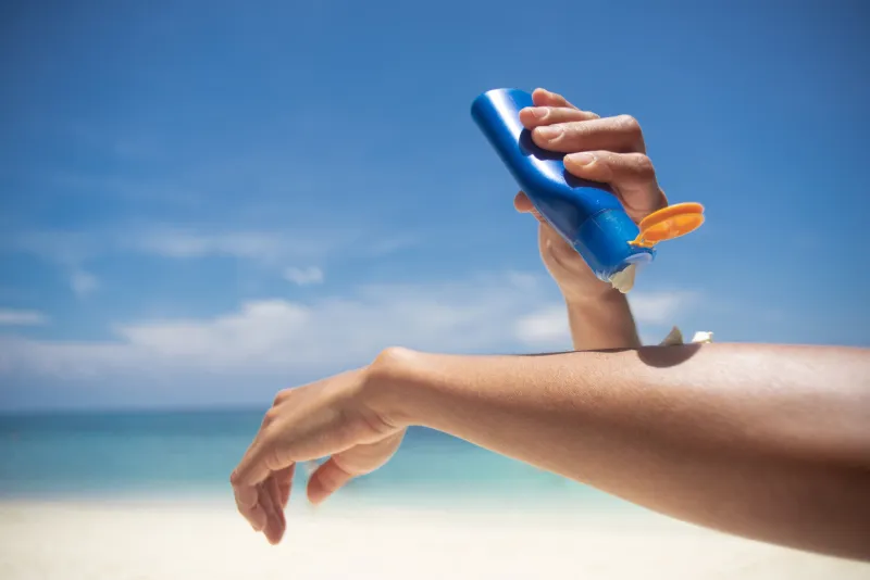 woman applying sunscreen on her hands from a bottle on the beach with the sea in the background spf sunblock protection conceptselective focus