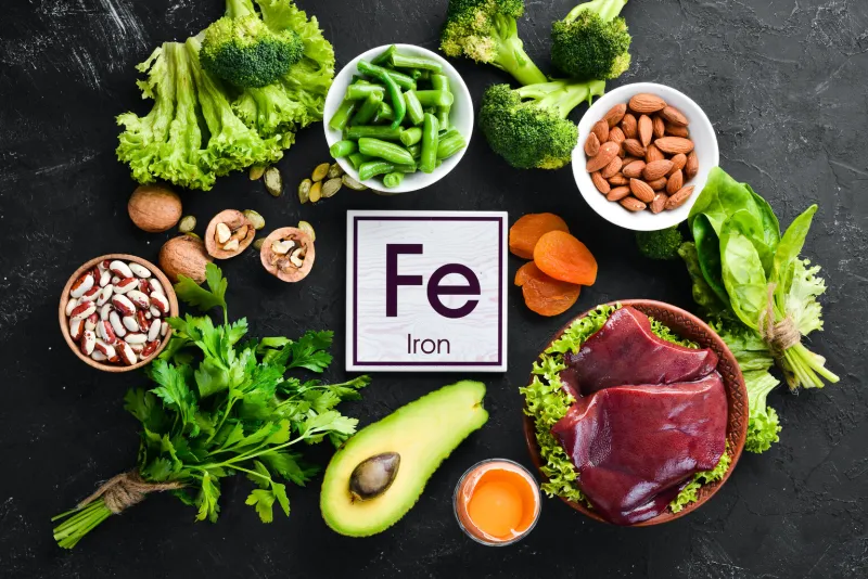 food containing natural iron fe  liver, avocado, broccoli, spinach, parsley, beans, nuts, on a black stone background top view