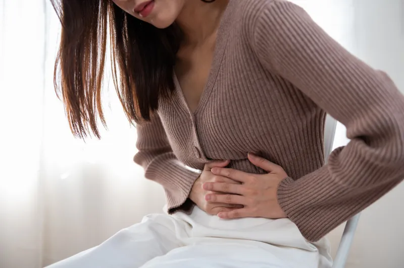 healthcare medical or daily life concept   close up stomach of young lady have a stomachache or menstruation pain sitting on a sofa