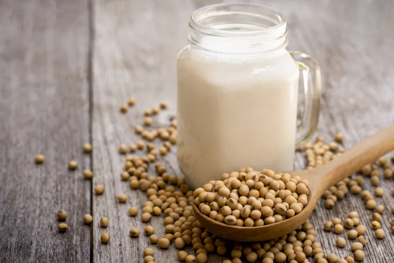 soy bean in wooden spoon and soy milk in glass jar isolated on wood table background