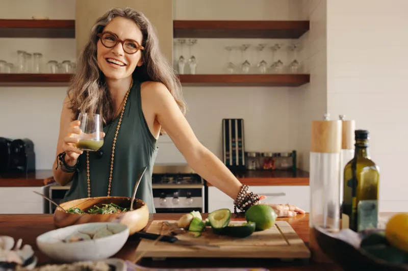 healthy senior woman smiling while holding some green juice in her kitchen mature woman serving herself wholesome vegan food at home happy woman taking care of her aging body with a plant-based diet