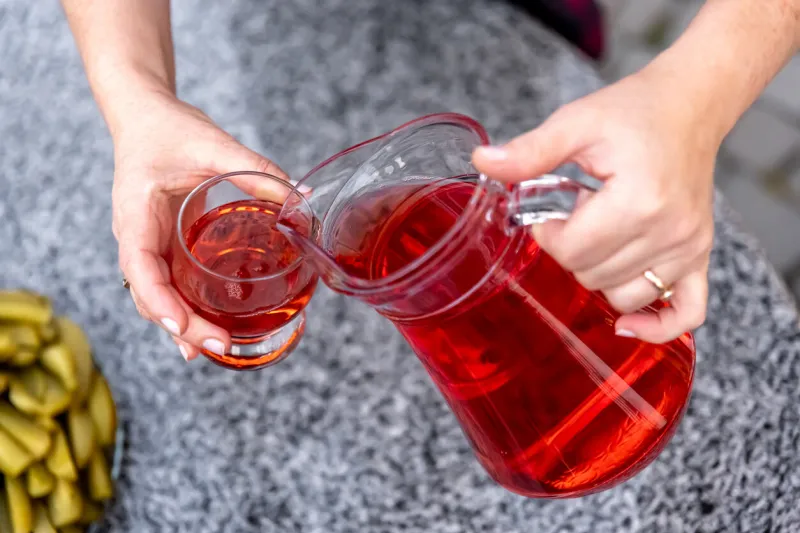 woman pouring healthy red cranberry juice from bottle into glass, close up