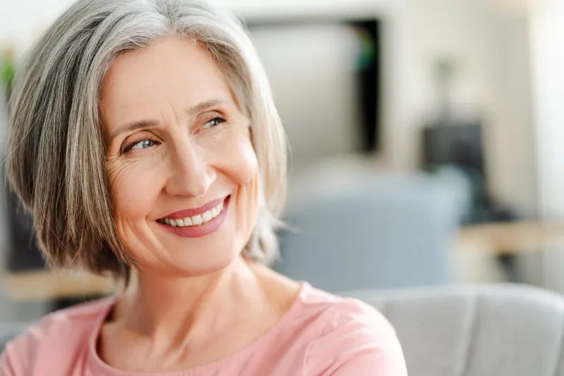 closeup portrait smiling confident senior woman sitting on comfortable sofa at home happy retired female with stylish gray hair, white teeth looking away natural beauty, healthy lifestyle concept