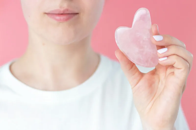 the girl holds a pink gua sha on a pink background front view