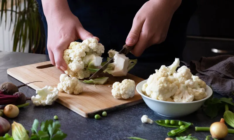 a woman cuts fresh cauliflower at the table