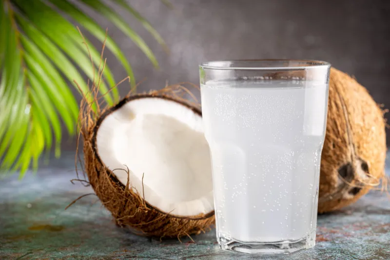 glass with fresh coconut water and coconuts on the table