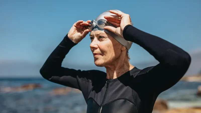 close up of a woman in swim wear standing near the sea female swimmer standing on the beach holding her swimming goggles on head