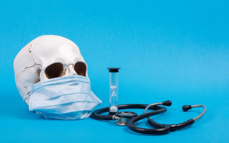 skull of a man in a protective mask, phonendoscope and watch on a blue background front view, place for text, copy space