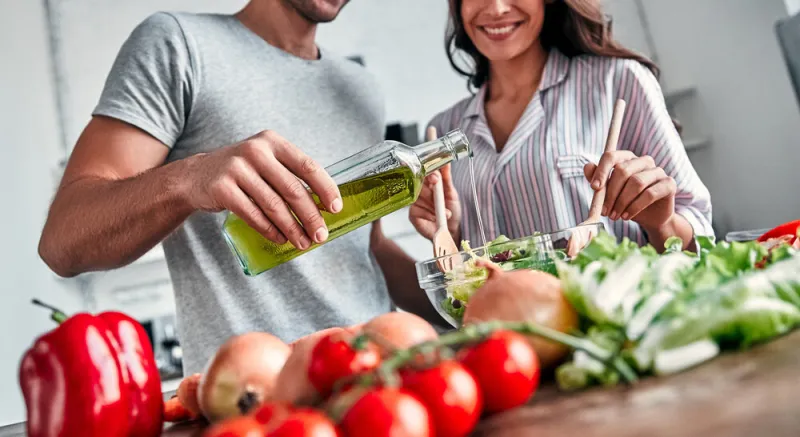 romantic couple is cooking on kitchen handsome man with a bottle of oil and attractive young woman are having fun together while making salad healthy lifestyle concept