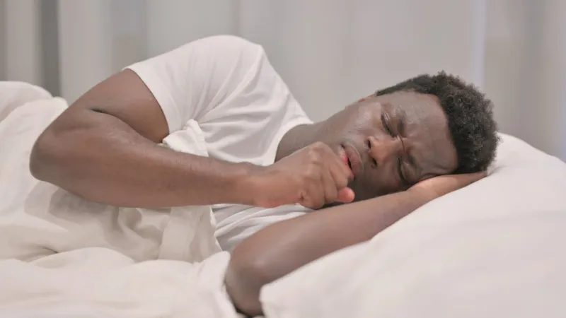 coughing african american man lying in bed on side