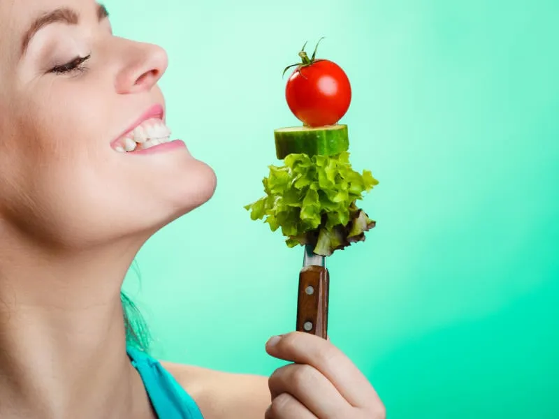 saine alimentation et régime concept closeup heureuse jeune femme tenant des légumes sur fond bleu studio tourné