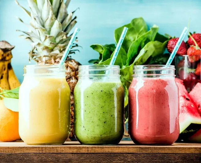 smoothies aux fruits fraîchement mélangés de différentes couleurs et goûts dans des bocaux de verre jaune, rouge, vert turquoise fond bleu