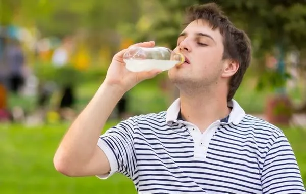jeune homme, boire de l'eau minérale dans le parc vert