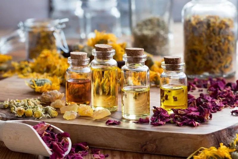 bottles of essential oil with dried rose petals, chamomile, calendula and frankincense resin on a wooden table