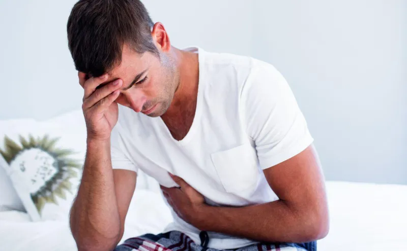 jeune homme assis avec douleur à l'estomac sur le lit