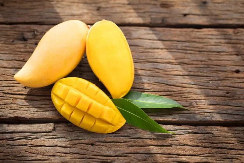 sliced ripe mango on wooded board with green leaves top-view