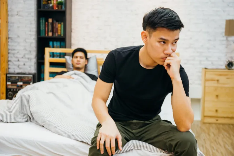 asian gay couple having argument with each other in bedroom thoughtful gay man having stress while another is sleeping - homosexual love concept