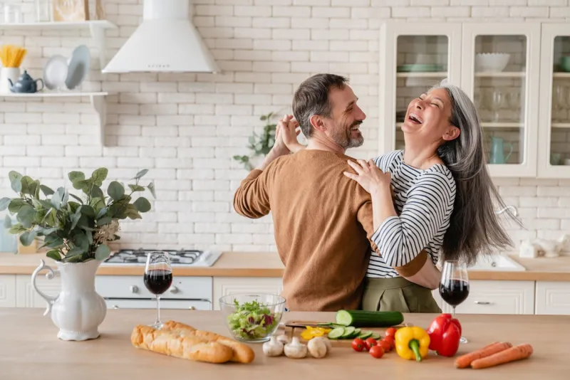 happy cheerful middle-aged mature couple family parents dancing together in the kitchen, preparing cooking food meal for romantic dinner, spending time together active seniors