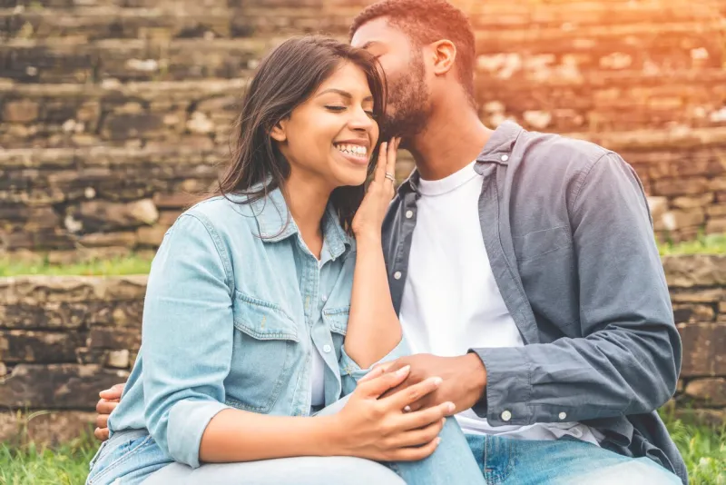 handsome man whispering to beautiful smiling woman how much he loves her as they are sitting in the park