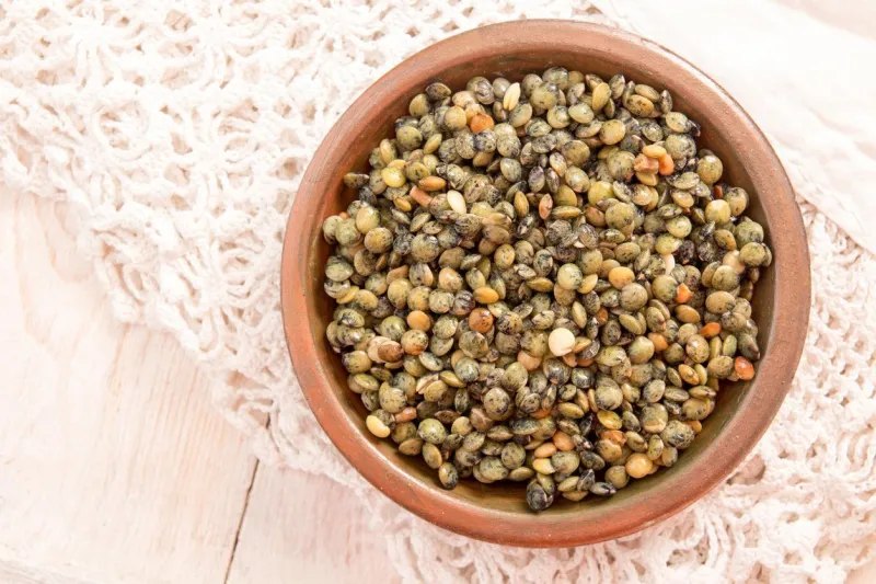 petite assiette avec lentilles vertes organiques crus sur nappe blanche dentelle sur une table en bois blanc