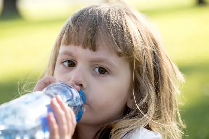 petite fille boit de l'eau et regarde la caméra