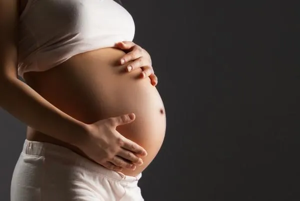 femme enceinte caresse son ventre sur fond gris