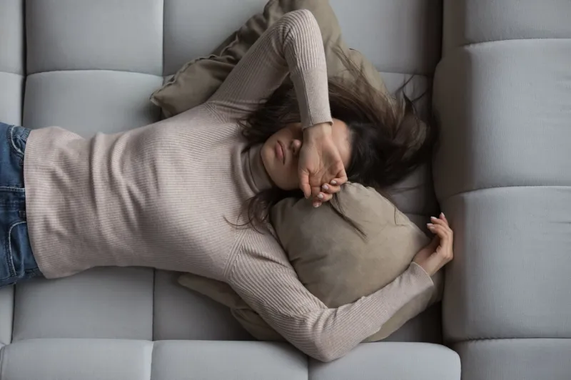 peaceful pretty 20s girl lying on back on comfortable couch at home, covering eyes with hand, sleeping at daytime, feeling tired, enjoying relaxation, leisure, break, weekend top view