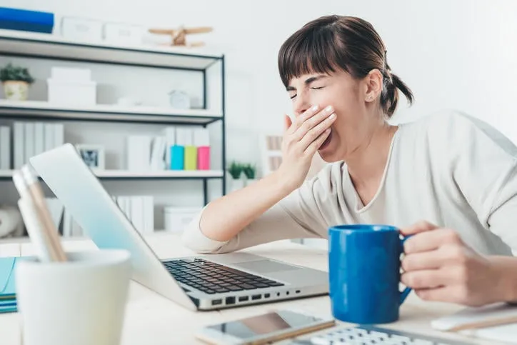 femme endormie fatiguée bâillement, travaillant au bureau et tenant une tasse de café, le surmenage et le concept de privation de sommeil